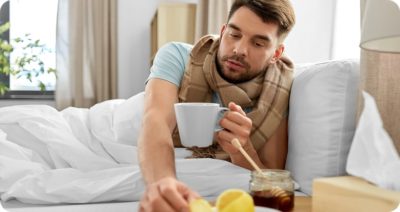 Uomo influenzato a letto che prende una tisana